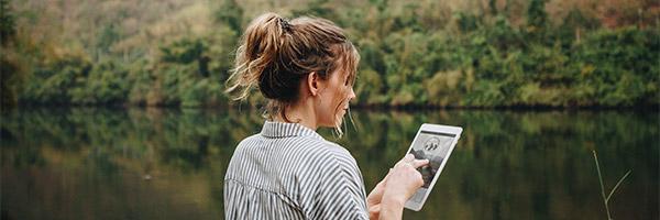 Préstamo Joven In - Una mujer usando una tableta digital en plena naturaleza Préstamo Joven In - Una mujer usando una tableta digital en plena naturaleza