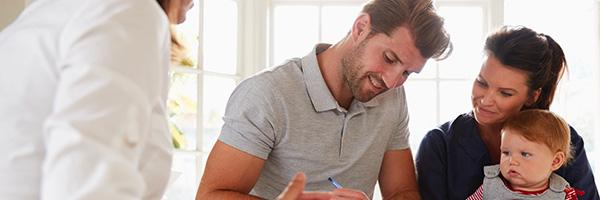 Simulador de Préstamos - Hombre con su mujer y bebe sonriendo en casa mientras que firman el contrato de un préstamo Simulador de Préstamos - Hombre con su mujer y bebe sonriendo en casa mientras que firman el contrato de un préstamo