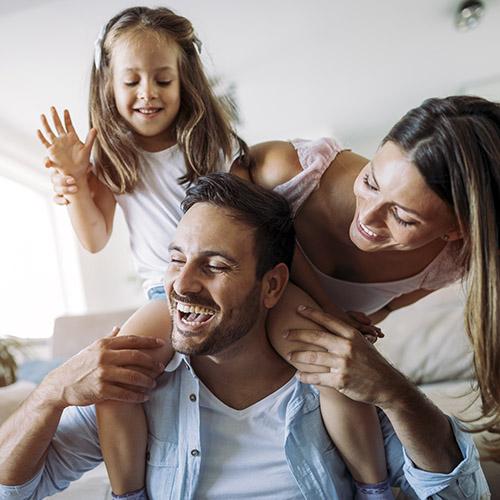 Más Seguros para Particulares - Familia joven con su hija felices y sonriendo mientras pasan un buen rato jugando en el salón de su casa