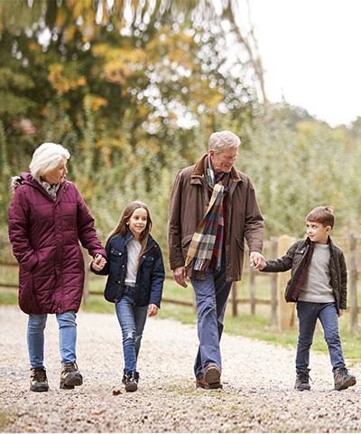 Ventajas para particulares - Abuelos con los nietos sonriendo mientras que caminan por el campo rodeados de árboles